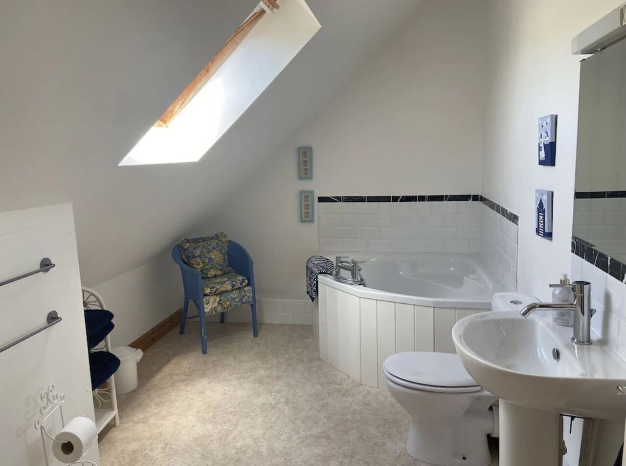 Une salle de bain avec une baignoire, des toilettes et un lavabo. On y trouve une chaise et un porte-serviettes.
