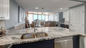 A modern kitchen with a granite countertop, stainless steel sink, and built-in dishwasher. - Seaside Haven | Beachfront | Panoramic Ocean Views (Port Aransas)