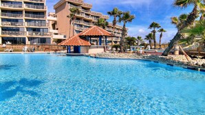 A swimming pool with a gazebo, palm trees, and a multi-story hotel building. - Seaside Haven | Beachfront | Panoramic Ocean Views (Port Aransas)