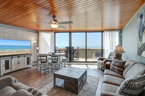 A spacious living area with a wooden ceiling, a large TV, a dining table, and a sofa.