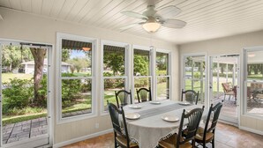 A dining area with a table set for four, surrounded by chairs, large windows, and a ceiling fan.