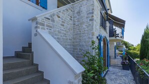 Un escalier en pierre mène à un bâtiment blanc doté de volets bleus et d’un balcon.