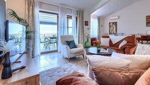 Un salon spacieux doté d’une grande télévision, de sièges confortables, d’un coin repas et d’un balcon aménagé avec du mobilier d’extérieur.