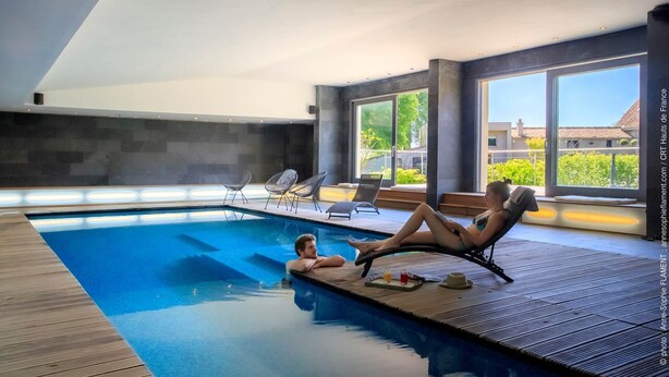 A modern indoor swimming pool with two lounge chairs and a small table.