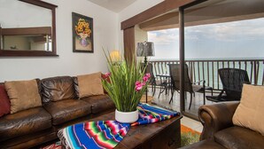 Un balcon avec vue sur l’océan, un canapé en cuir, un tapis coloré et une plante en pot.