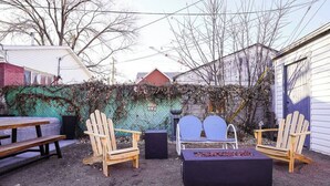An outdoor seating area with wooden chairs and a bench, surrounded by a garden and a fence.