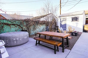 A patio with a wooden table and bench, surrounded by a green fence and a white building.