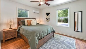 A bedroom with a bed, nightstand, ceiling fan, and large windows.