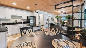 A modern kitchen with white cabinets, a black refrigerator, and a dining area with a dark wooden table and woven placemats.