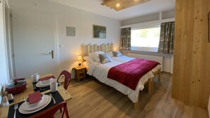 A bedroom with a wooden ceiling, a bed with white bedding, a red blanket, a bedside table with a lamp, and a window with curtains. - La Marmotte (Siviez)