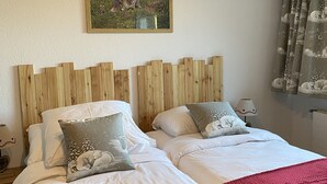 A double bed with white linens and a red blanket, a wooden headboard, and a painting of a dog on the wall. - La Marmotte (Siviez)