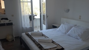 Ein Hotelzimmer mit Bett, Nachttisch, Fenster mit Vorhängen und Blick ins Freie.