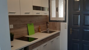Eine moderne Küche mit weißen Schränken, einer grünen Schneidebrett, einer Spüle und einer dunkelholz-Rückwand.