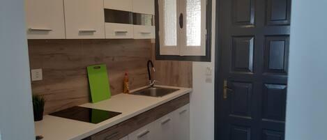 A modern kitchen with white cabinets, a green cutting board, a sink, and a dark wooden backsplash.
