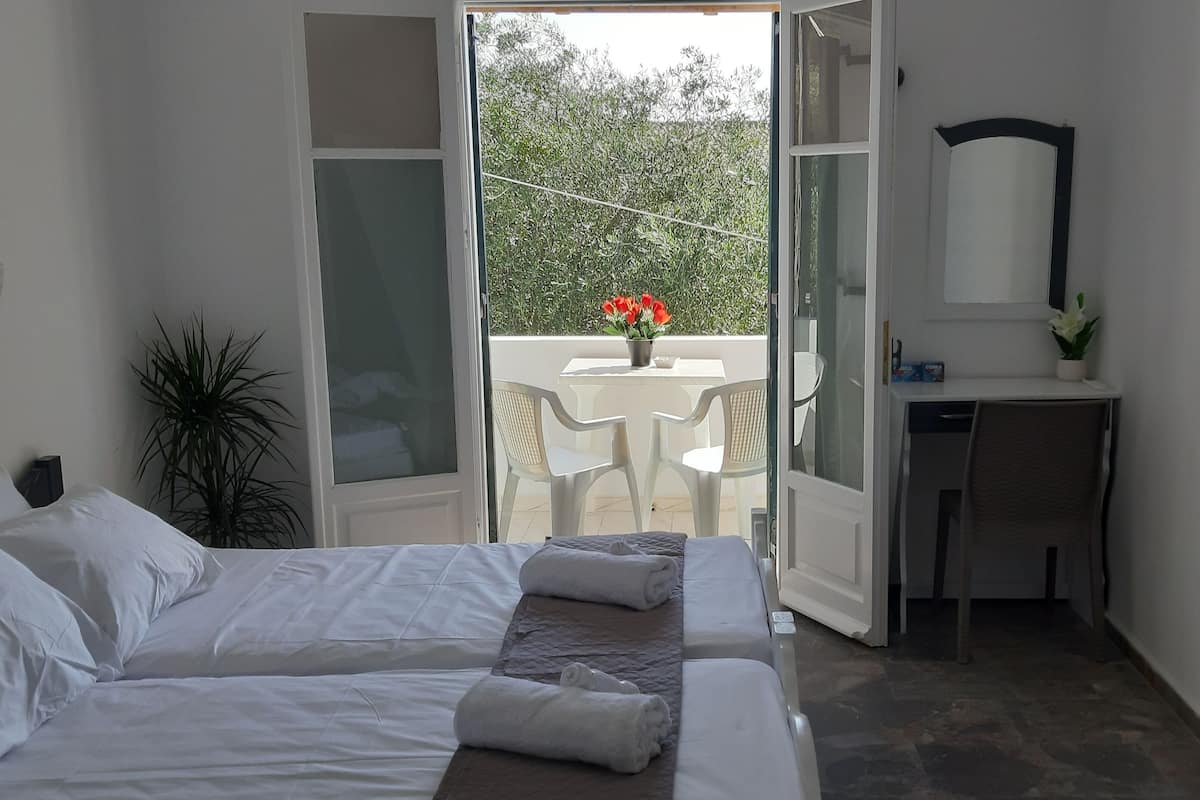 A bedroom with a bed, a bedside table, a mirror, and a view of a balcony with a table and chairs.