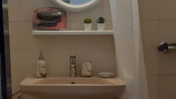 A bathroom with a pedestal sink, a mirror, a shelf with toiletries, and a shower curtain.