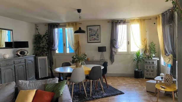 A living room with a sofa, a dining table with chairs, a kitchen area, and a small table with a plant. - Holiday home in Périgord (Saint-Georges-de-Montclard)