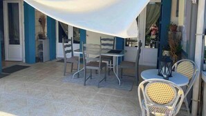 An outdoor patio with a table and chairs, a covered area, and a view of the building's interior. - Holiday home in Périgord (Saint-Georges-de-Montclard)