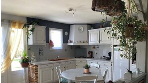 A kitchen with white cabinets, a dining table with chairs, and potted plants. - Holiday home in Périgord (Saint-Georges-de-Montclard)