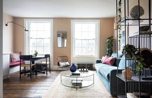 A living room with a sofa, a coffee table, a chair, and a radiator. There are two windows and a mirror on the wall. - Luxurious Apartment - minutes from Angel Tube St. (London)