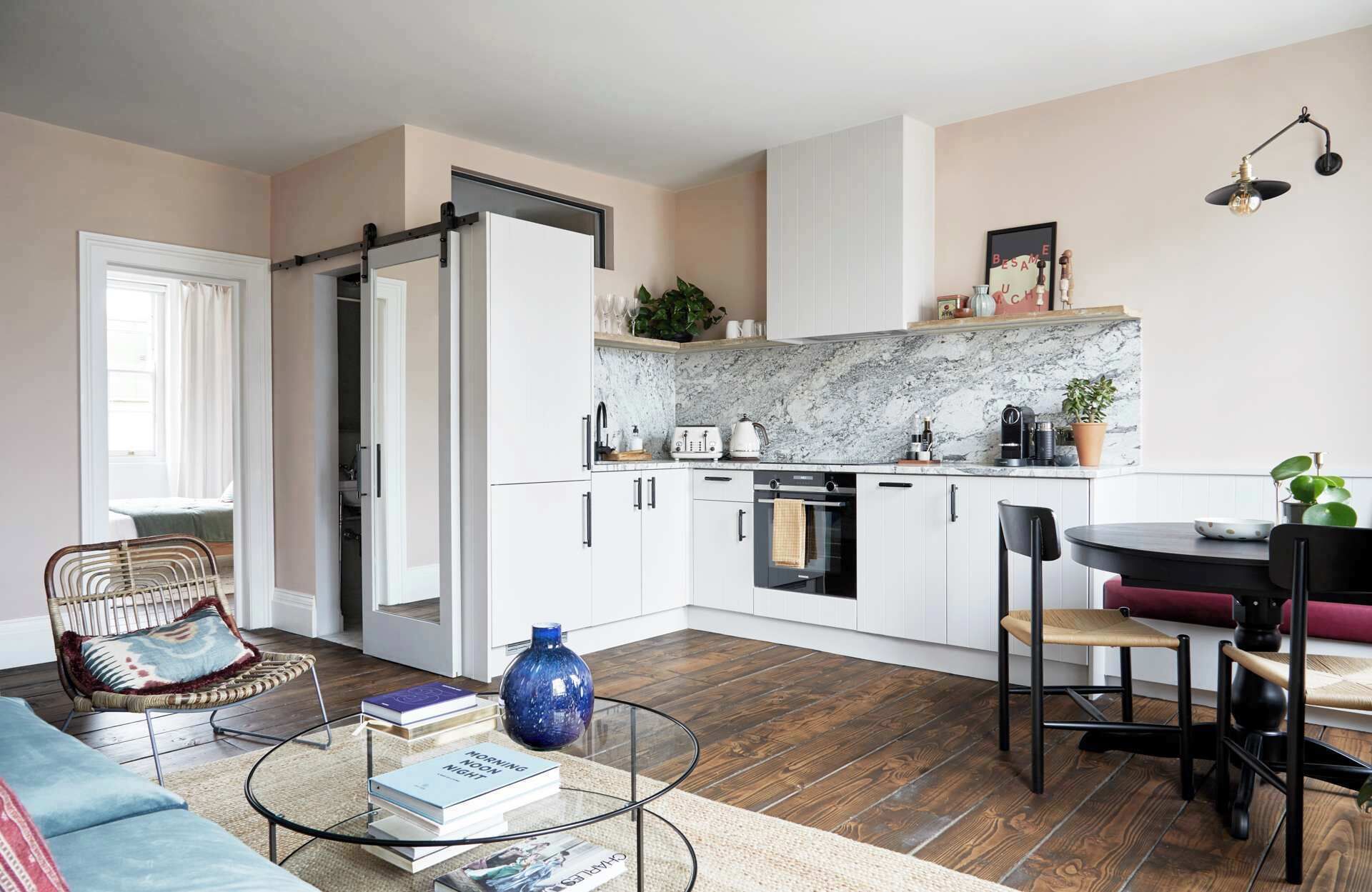 Una cucina moderna con mobili bianchi, zoccolo in marmo e zona pranzo con tavolo e sedie rotonde.