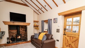 A cozy living room with a fireplace, a brown leather sofa, a wooden door, and a flat-screen TV mounted above the fireplace. - The Old Cobblers Shop (Llandrindod Wells)