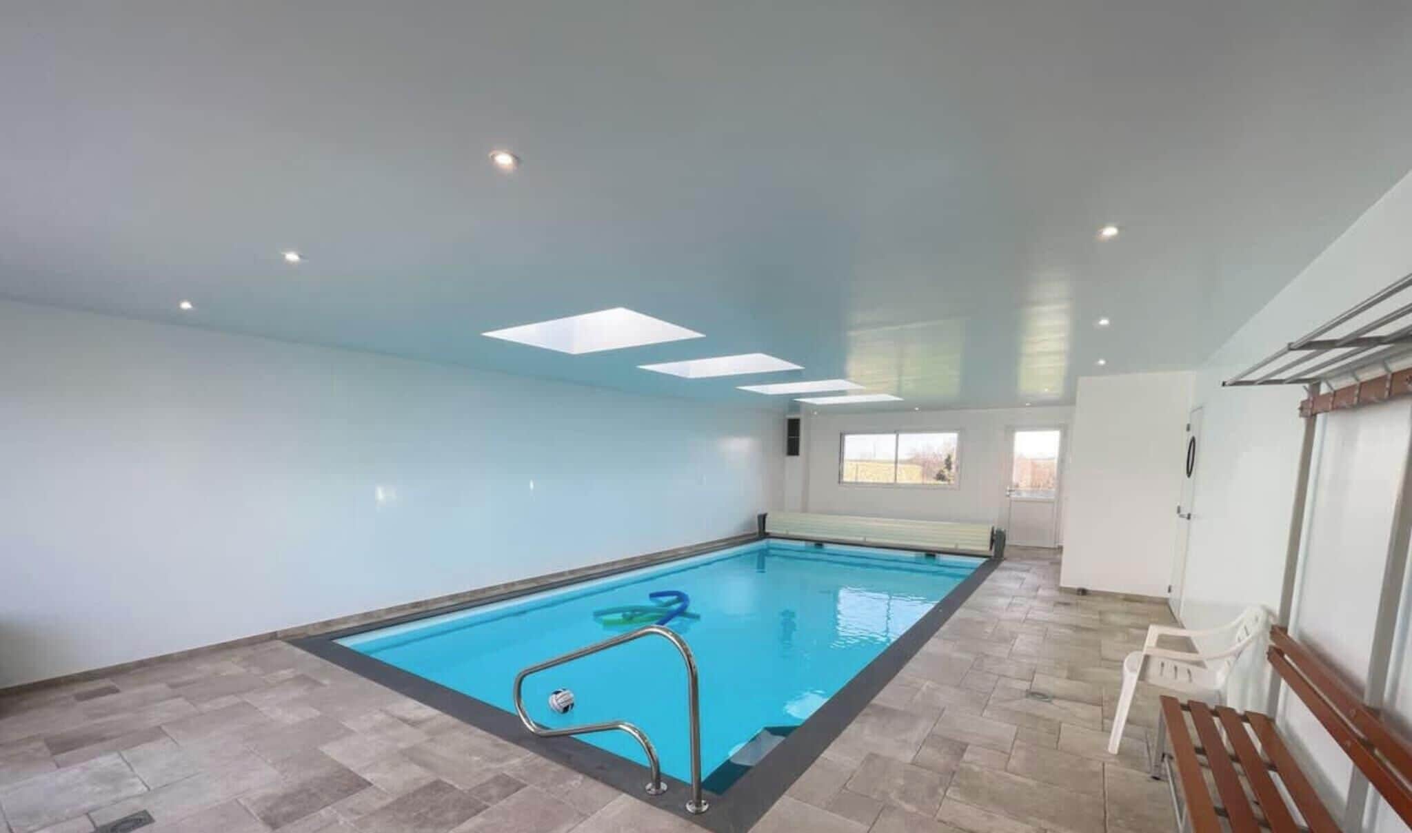 Une piscine intérieure avec un sol carrelé, un escalier et un banc.