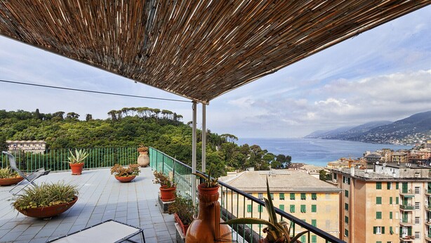 A balcony with potted plants, a metal chair, and a view of the sea and cityscape. - Stunning Sea View Apartment by Wonderful Italy (Camogli)