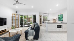 Ein modernes Wohnzimmer mit einer Couch, einem Couchtisch und einem Fernseher. Es gibt einen Essbereich mit Tisch und Stühlen. Die Küche ist mit einer Mikrowelle und einem Schrank ausgestattet.