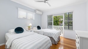 Ein Schlafzimmer mit zwei Betten, einem Deckenventilator, weißen Wänden und einem Fenster mit Jalousien.
