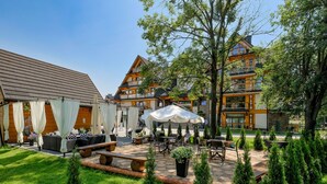 Pátio de hotel com área de estar externa, espaço coberto e jardim bem cuidado.