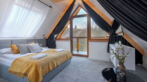 Quarto com cama, mesa de cabeceira, janela com cortinas e vista para o exterior.