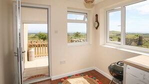 A room with a large window, a door leading outside, a ceiling fan, a washing machine, and a view of the countryside.