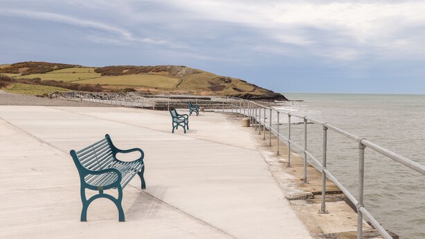 A coastal walkway with benches and a railing overlooking the sea.