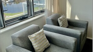 Une pièce avec deux fauteuils gris et une vue sur un lac où l’on peut voir des bateaux.