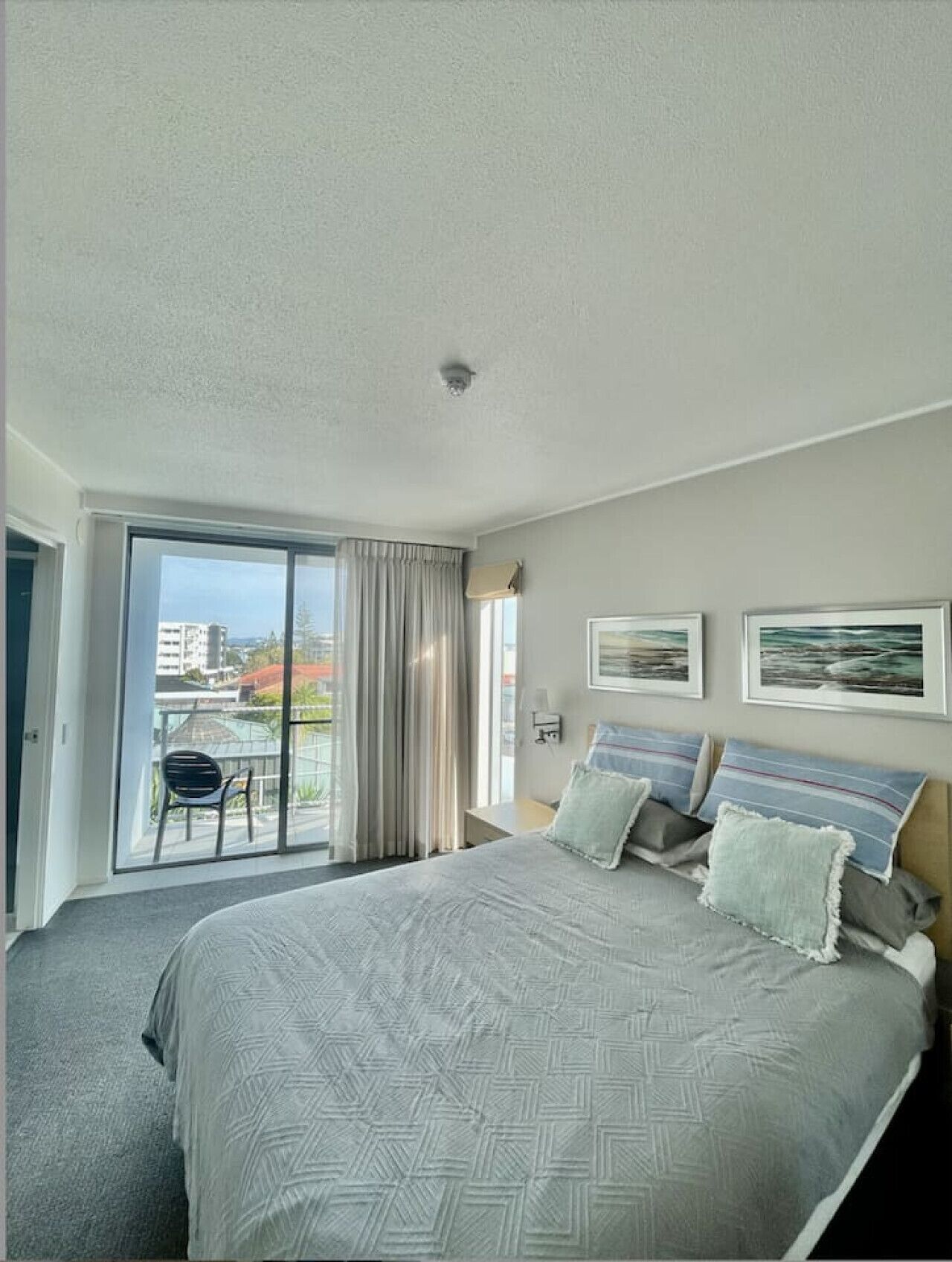Habitación de hotel con una cama grande, vista a la ciudad por la ventana y un balcón con una silla.