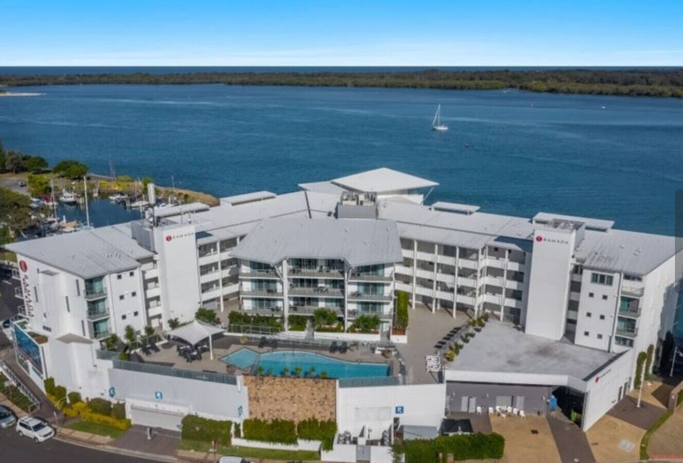 Et moderne hotel med central pool, flere altaner og udsigt til vandet.