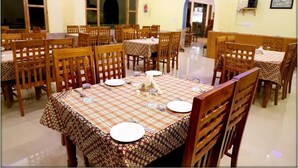 A dining area with multiple tables and chairs, each set with plates, cutlery, and glasses. - The Ranikhet Continental (Ranikhet)