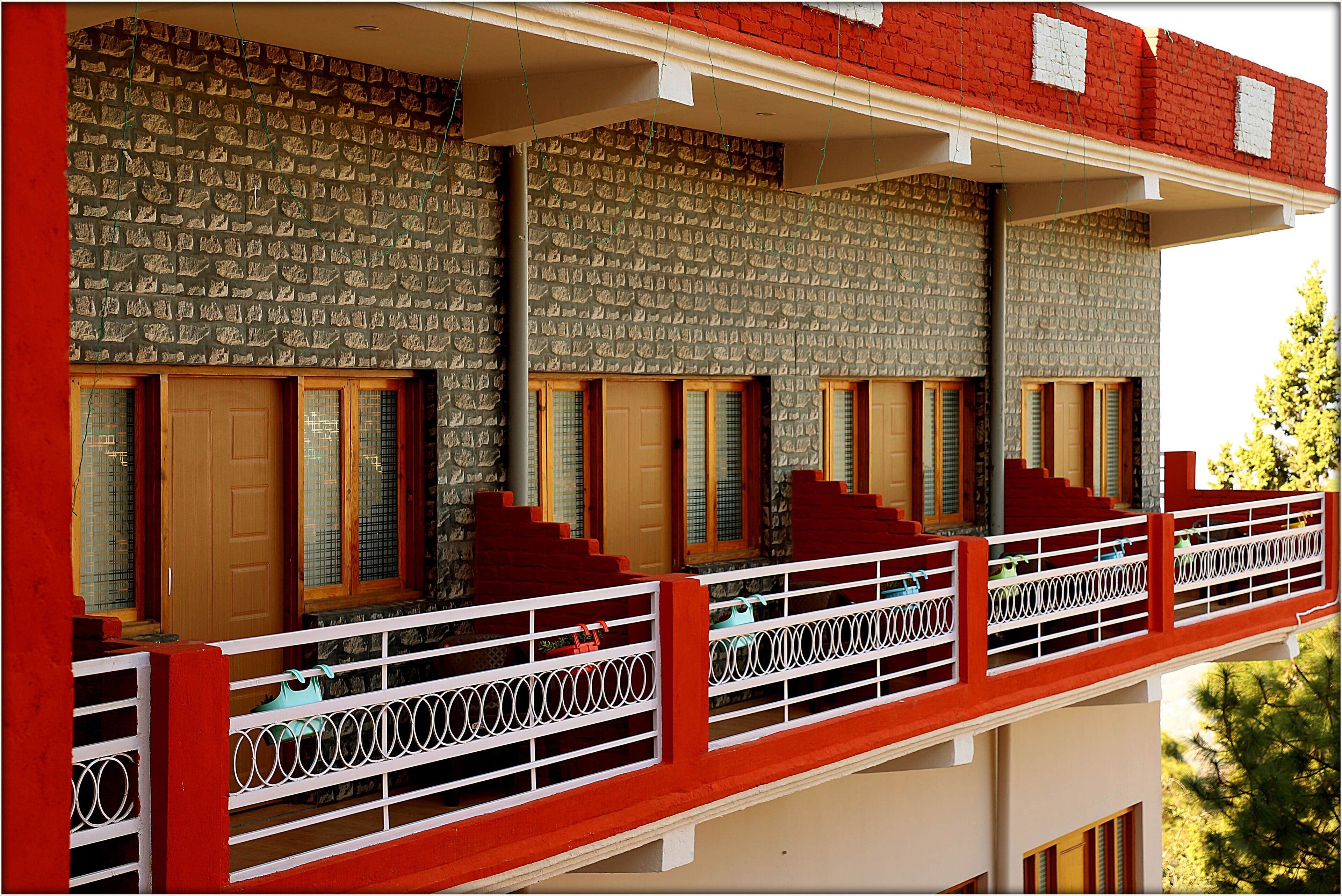 A multi-story building with a red and white exterior, featuring a balcony with a white railing and a series of windows with wooden shutters.