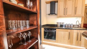 A modern kitchen with wooden cabinets, a built-in oven, and a countertop with a coffee maker and utensils. - The Upper Room (Ballymena)