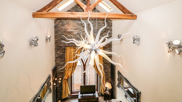 A spacious hallway with a high ceiling, exposed wooden beams, a unique chandelier, and a staircase leading to another level. - The Upper Room (Ballymena)