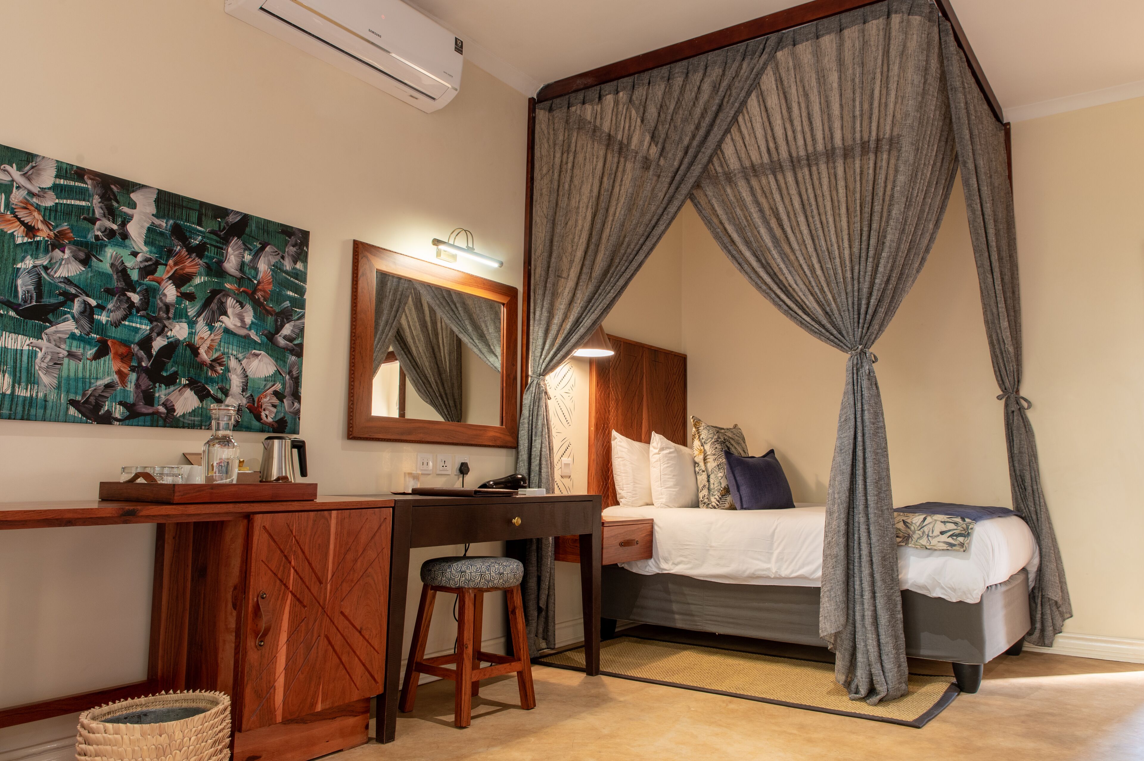 A bedroom with a canopy bed, a desk with a chair, a bedside table, and a wall-mounted air conditioner.