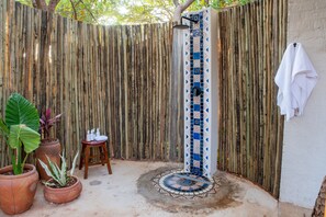 A shower with a blue and white tile design, a wooden fence, and a towel hanging on a wall. - Shongwe Oasis (Victoria Falls)