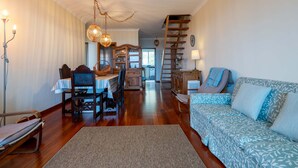 Un salon chaleureux avec un escalier en bois, un coin repas avec une table et des chaises, et un canapé à motifs.