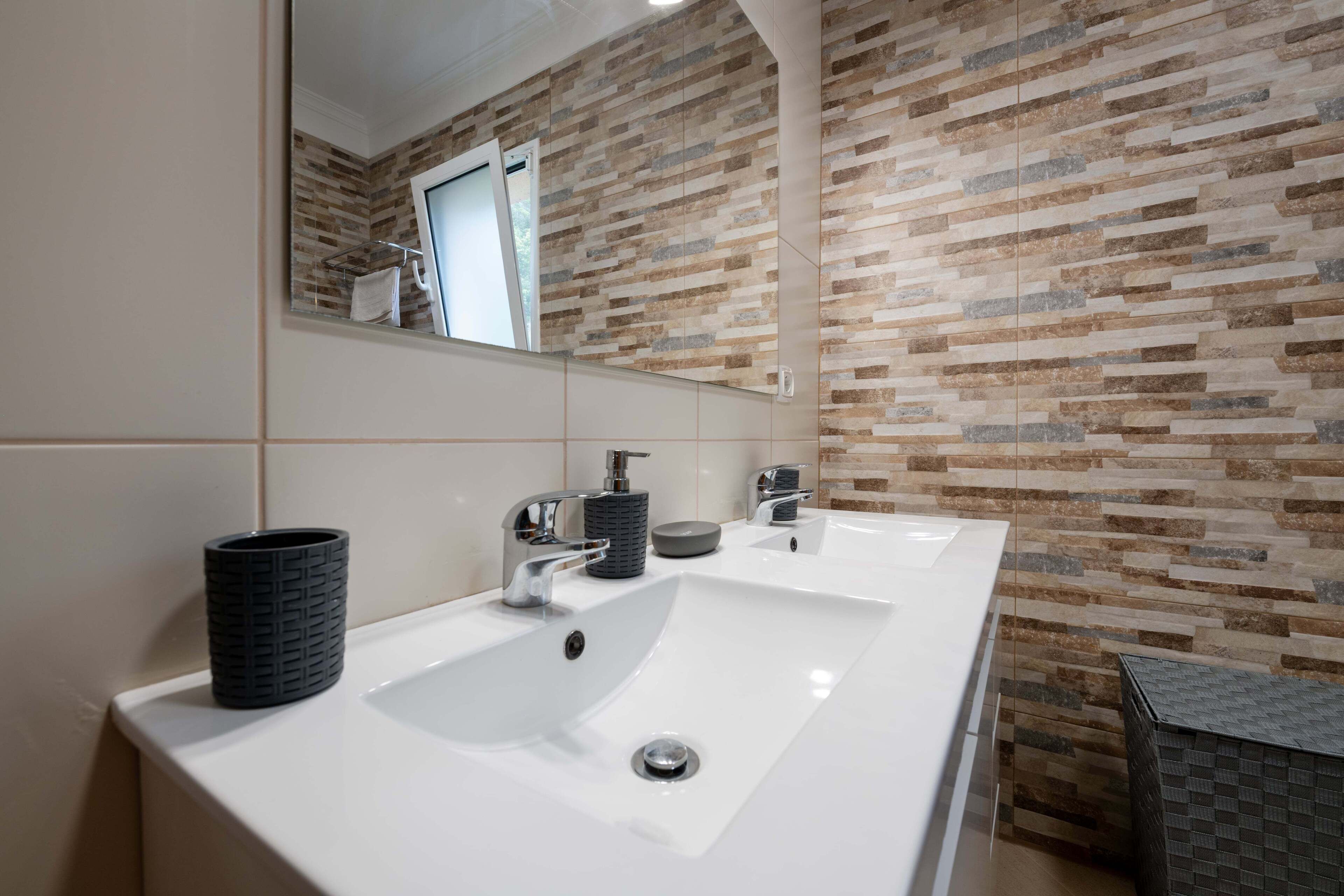 A modern bathroom with two sinks, a large mirror, and a textured wall.