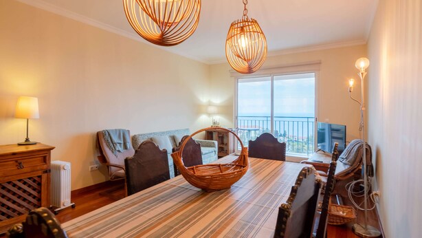Un espace repas comprenant une longue table, des chaises, un panier en osier et des lampes suspendues.