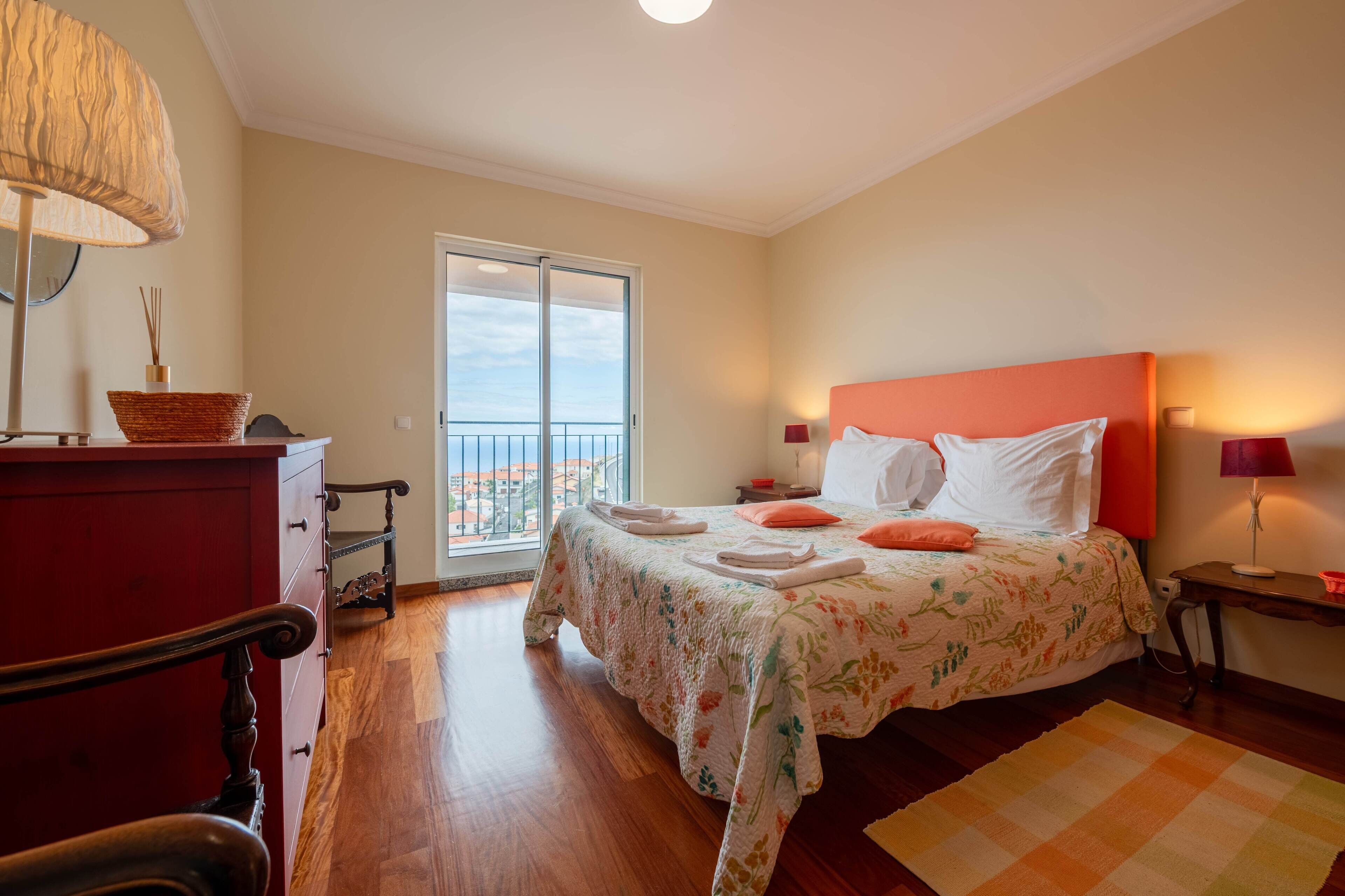 Une chambre d’hôtel avec un lit, une commode, une lampe et une vue sur la ville, accessible par une porte-fenêtre donnant sur un balcon.