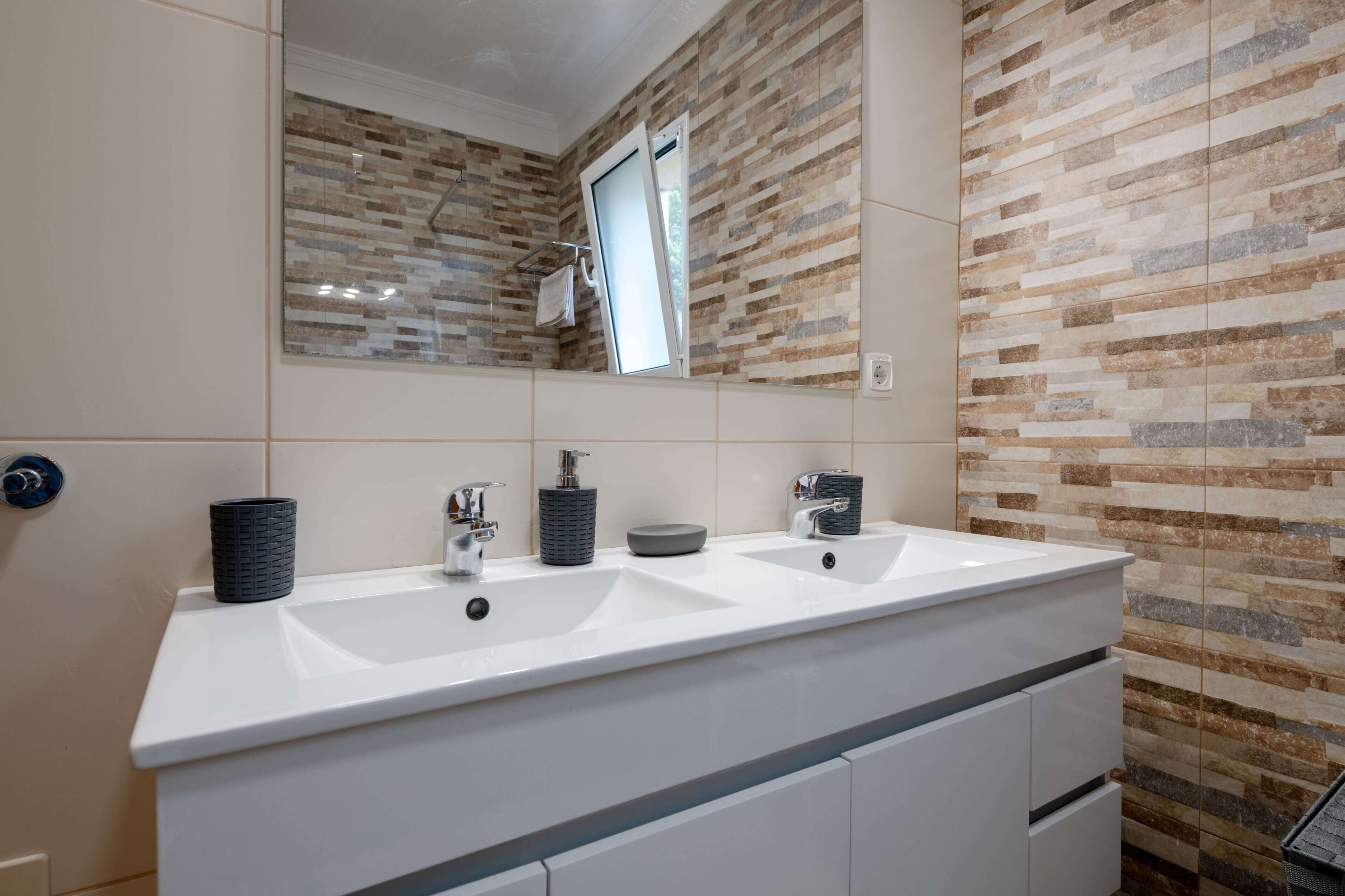 Une salle de bain avec deux lavabos, un miroir et un mur recouvert de carreaux.
