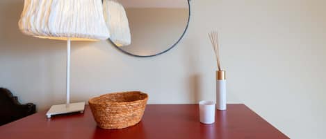 A red table with a white lamp, a woven basket, a white candle, and a mirror.