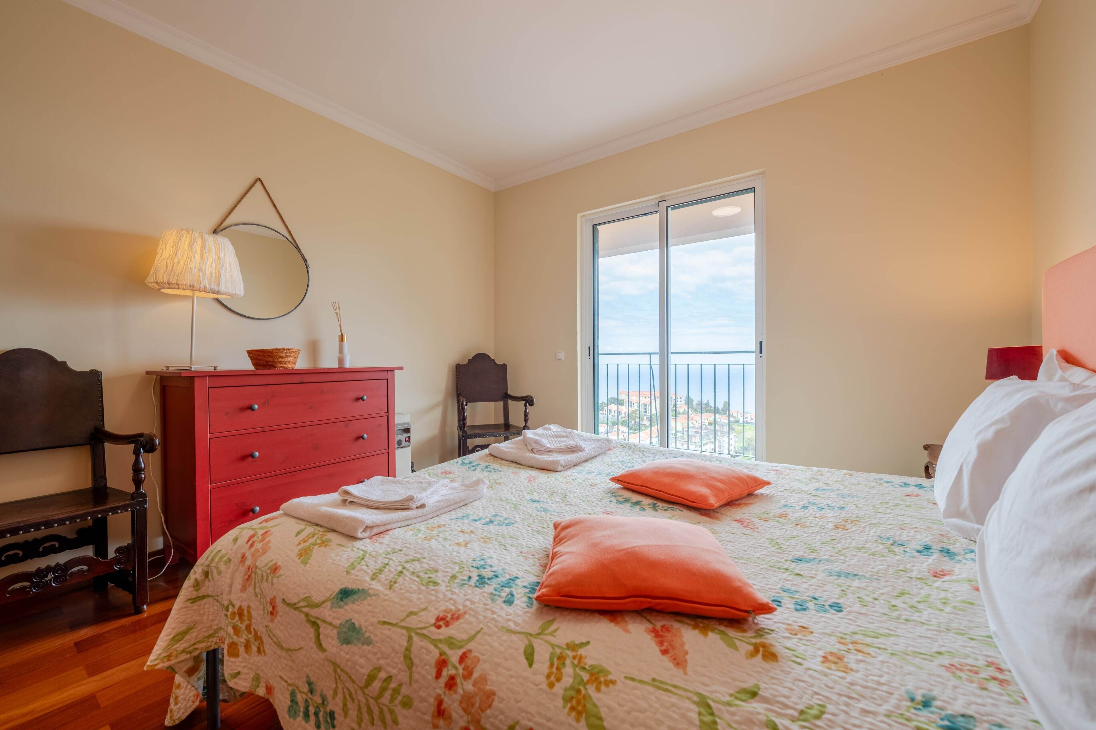 A bedroom with a bed, a dresser, a chair, and a window with a view.